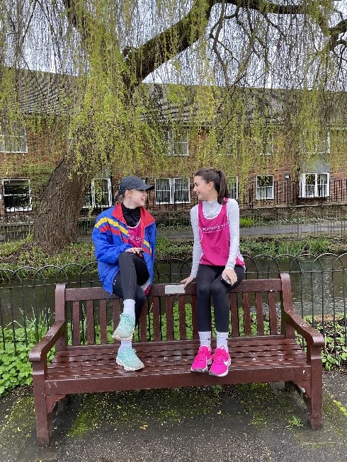 Two woman sitting on a bench talking by a river.