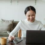 An image of a woman smiling while working on a laptop.