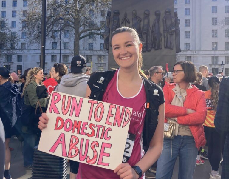 Marathon runner smiling and holding a sign that says Run to End Domestic Abuse