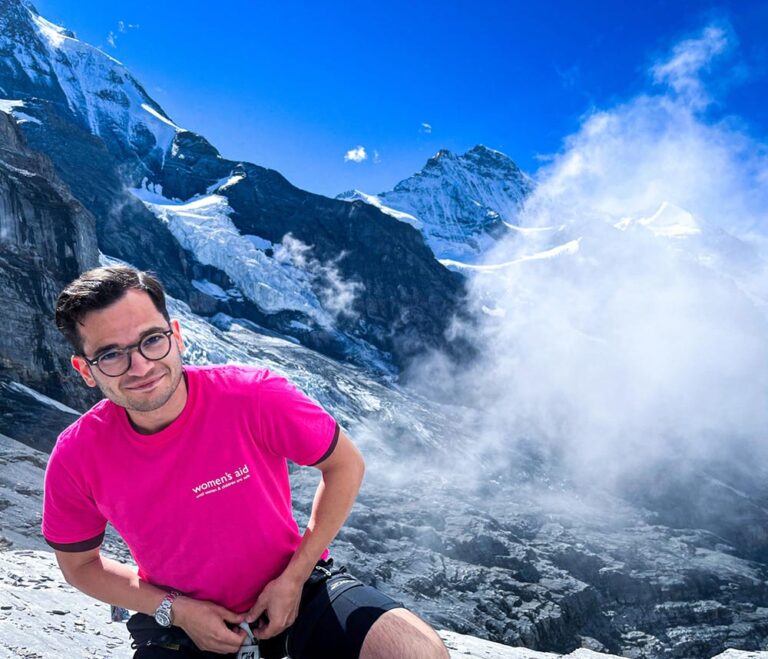 Man wearing pink Women's Aid t-shirt sitting in the mountains