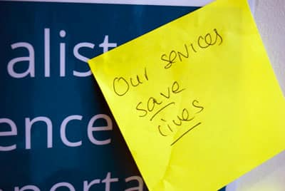 Yellow post-it note that has written: 'Our services save lives'