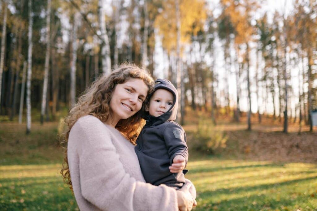 Woman holding a child standing in front of trees and woodland