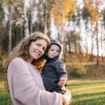 Woman holding a child standing in front of trees and woodland