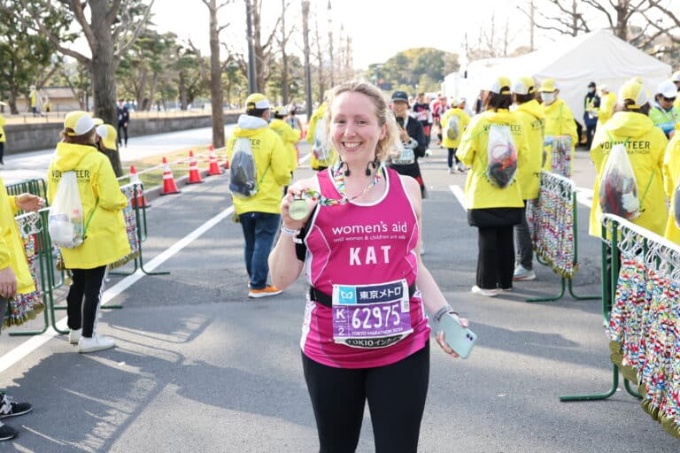 A photo of a fundraiser holding a medal in a Women's Aid running vest.